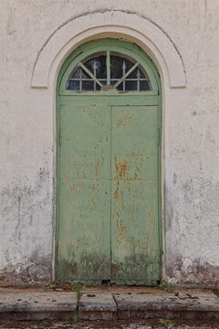 Arched doorway featuring a weathered green metal door set into a light-colored, textured plaster wall, Muhu, Estonia, Europe.
