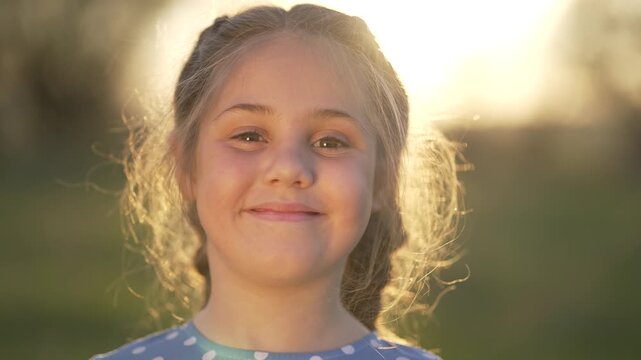 Girl smiling in outdoor field with sunlight and backlight, child portrait showing happy smile, loose hair catching sun, nature setting with warm glow, child face expressing joy and natural happiness