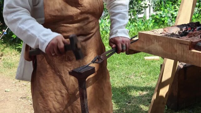 Blacksmith in traditional attire skillfully forges red-hot metal piece outdoors using hammer and anvil, ancient craft of metalworking and manual labor. craft heritage, industrial skill.