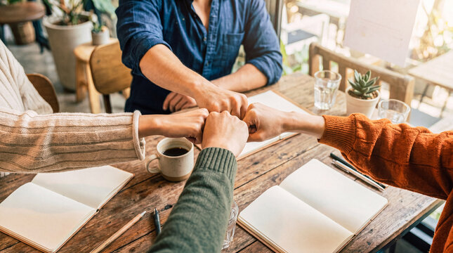 Photograph of diverse team members doing a fist bump over a wooden desk, symbolizing collaboration and unity.