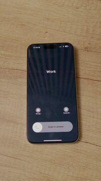 Vertical Screen: A smartphone rings with an incoming work call. The phone is placed on a wooden table. It shows the caller ID as Work, indicating a business-related matter.
