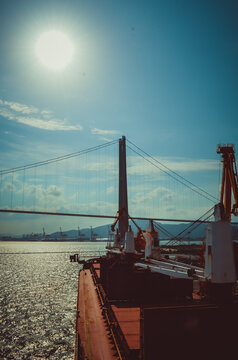 Cargo ship alongside port terminal with suspension bridge in background in South Korea. Industrial shipping, logistics and global trade concept.