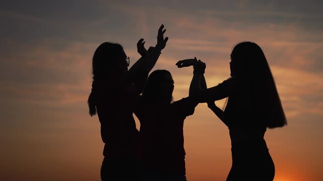 Dancing silhouette trio at sunset three women dance under orange sky at dusk each woman raising hand in fluid movement group friendship and quiet joy visible in silhouette against warm horizon