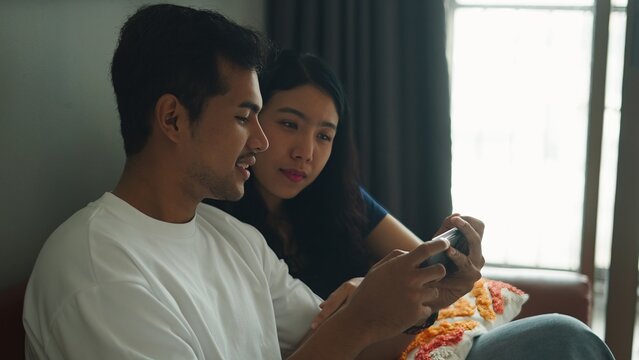 Happy couple using smartphone together, enjoying leisure time at home