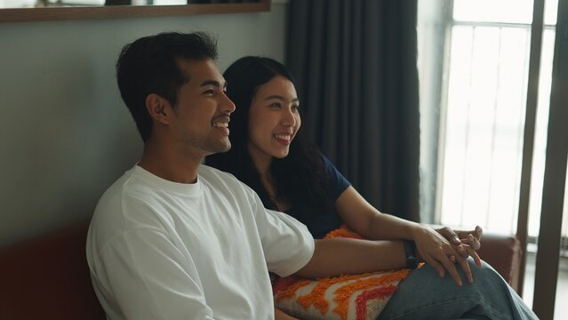 Affectionate couple relaxing, holding hands and watching tv while cuddling on living room couch, sharing tender moment together