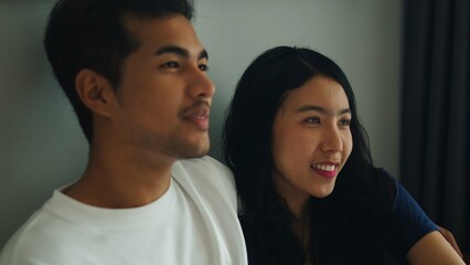 Fototapeta premium Young asian couple enjoying time together, watching television in their living room