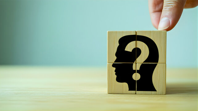 A hand is placing a final puzzle piece, a wooden cube with a question mark and human head silhouette, into a larger puzzle representing a mystery or unknown thought