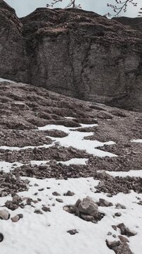 Ripido pendio montano con rocce scure e chiazze di neve, immerso in un&rsquo;atmosfera fredda e nuvolosa che richiama la transizione stagionale tra inverno e primavera