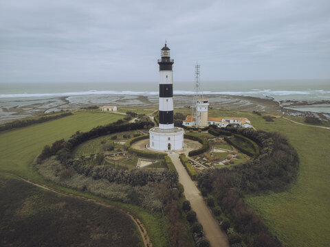 Aerial view of the picturesque Phare de Chassiron lighthouse on a serene coastline with ocean waves, Saint-Denis-d'Oleron, Charente-Maritime, France.
