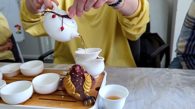 Traditional chinese tea ceremony gongfu cha with white ceramic teapot, cups and golden money frog on bamboo tray. Pouring oolong tea, mindful atmosphere, oriental culture and zen lifestyle.