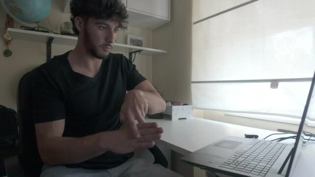 Young man speaks sign language on a video call on a laptop indoors. 