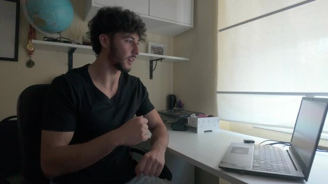 Young man speaks sign language on a video call on a laptop indoors. 