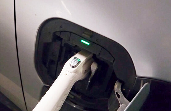 Electric Vehicle Charging at Underground Parking Station. Close-up of a white charging cable plugged into an electric car in a dimly lit underground parking garage. Concept of eco-friendly transport