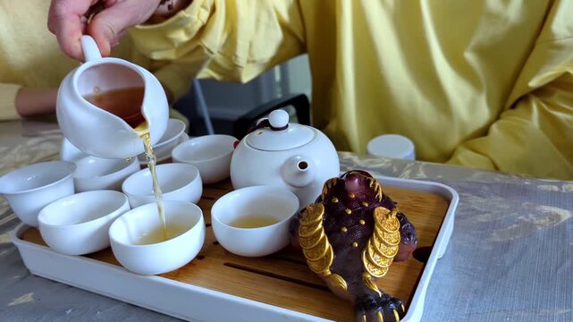 Traditional chinese tea ceremony gongfu cha with white ceramic teapot, cups and golden money frog on bamboo tray. Pouring oolong tea, mindful atmosphere, oriental culture and zen lifestyle.