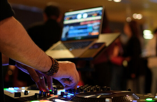 DJ Mixing Music on Professional Controller in Nightclub. Close-up of a DJ's hand adjusting knobs and faders on a professional mixing console. Blurred red bokeh lights in the background