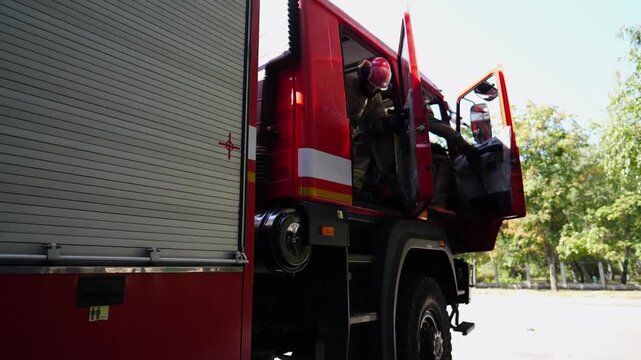 Male firefighters opening doors of cabin and fast exiting from passenger seats of red truck. Professional young firemen running to the place of a fire. Concept of saving lives and heroic profession