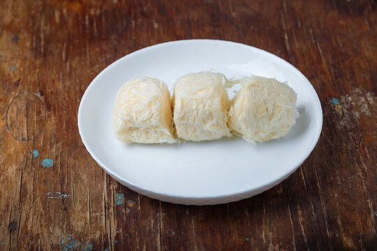 Pismaniye, cotton candy or dragons beard with vanilla taste on white plate, wooden background. Turkish dessert, light halva, candy floss. Copy space
