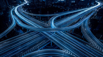 Striking long exposure aerial photograph of a complex highway interchange with blurred car light trails at night. © Satvinder