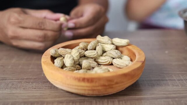 A man and his daughter are eating peanuts. Close up of peanuts on the table.