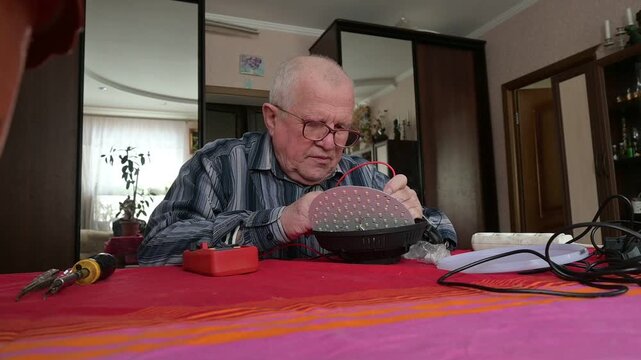 Senior Technician or Hobbyist Repairing Modern LED Ceiling Lamp at Home Table with Multimeter and Hand Tools