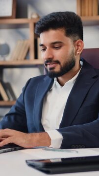 Indian ethnic businessman sitting at desk using laptop computer. Happy businessman sitting at remote workplace with laptop. Top manager working in office. Slow motion.