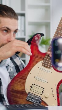 Young man guitar teacher talking to camera and showing how play, blogger man create tutorial lesson for beginners, string instrument class for internet auditory. Slow motion