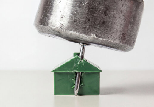 Nail driven through miniature plastic house by hammer, construction  and building costs problem concept