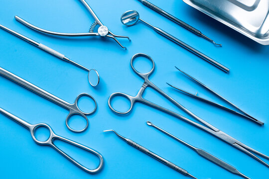 Pattern flat lay of stainless surgical instruments and tools on blue table, top view. Medical background