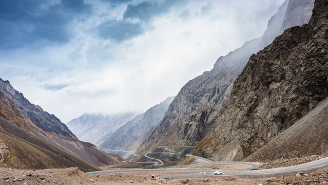 Dramatic view of the iconic Duku Highway, famed as China's Most Beautiful Road, winding through mist-shrouded, towering autumn mountains in Xinjiang. A car charges headlong into the fog-shrouded peaks