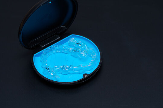 Orthodontic invisible braces aligner inside blue retainer case in dark background