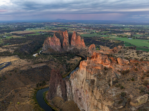 Aerial view of Smith Rock State Park featuring towering volcanic rock formations and the winding Crooked River under a cloudy twilight sky in Crooked River, Oregon, United States.