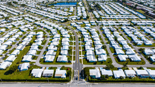 Aerial view of a dense grid of white-roofed houses intersected by straight roads, creating a stark geometric pattern against the green foliage, Florida, United States.