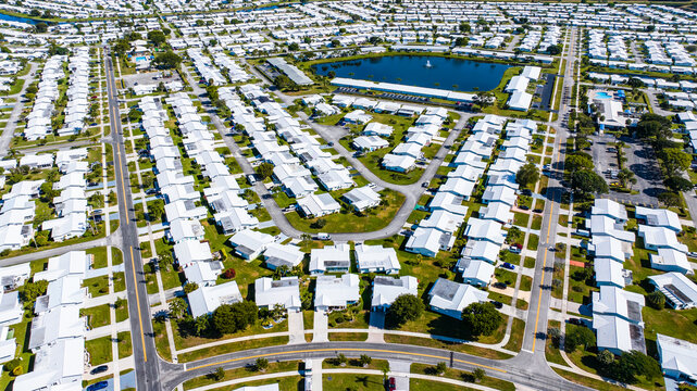 Aerial view of a dense residential area with white roofs contrasting against the green lawns and streets, near a small lake, Florida, United States.