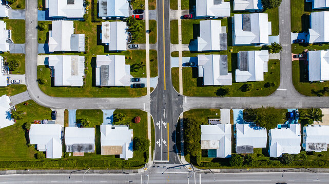Aerial view of bright white roofs contrasting with the lush green lawns and dark asphalt streets of a meticulously planned neighborhood, Florida, United States.