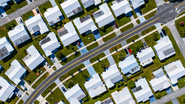 Aerial view of compact houses with white roofs, neatly aligned along streets with cars parked outside, a grid of modern suburban living, Florida, United States.