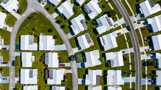 Aerial view of houses with white roofs stand in orderly rows amidst green lawns, bisected by curving streets, creating a tranquil and geometric landscape, Florida, United States.