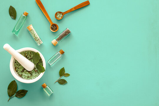 Homemade organic cosmetics products - tea tree essential oil and sea salt in mortar and pestle with green leaves on green background, top view.