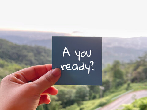 Hand holding note with &ldquo;are you ready&rdquo; message against scenic road and nature background, motivation concept