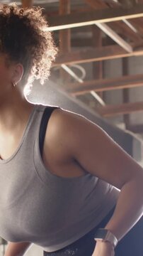 Vertical video: Tilting camera revealing woman in gray tank leaning at gym with rods for workout