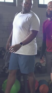 Vertical video: Entering gym, men in red and white shirts walking by dumbbells, preparing workout