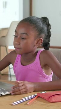 Vertical video: Glancing left, child in pink top using laptop pad at table, learning with pencils