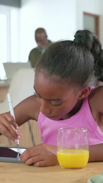 Vertical video: Picking up white stylus, child in pink top drawing on tablet at home, orange juice
