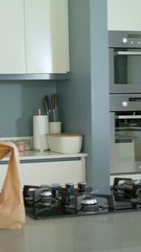 Mother placing grocery bags, pink-top child reaching, unpacking mesh bag for stocking kitchen