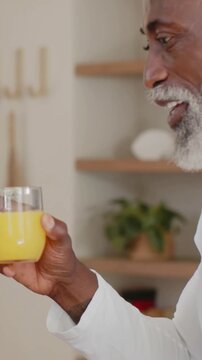 Vertical video: Replying offscreen, man in white top holding juice glass in kitchen, copy space