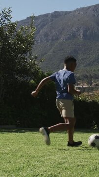 Vertical video: Dribbling from crouch, boy in blue tee running yard with ball to goal, dad blocking