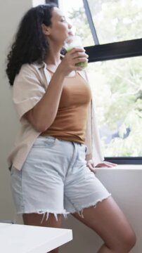 Vertical video: Sipping green juice, model in top by window with camera panning, prepping ringlight