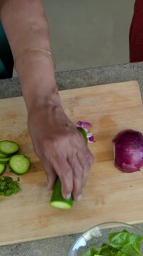 Vertical video: Starting prep, senior in green slicing cucumber, chopping herbs on board in kitchen