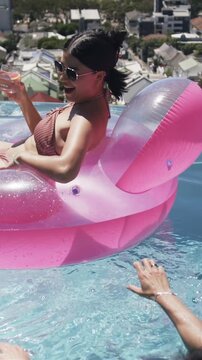 Vertical video: Woman reclining on pink float with glass, shifting toward reaching arm in travel ad