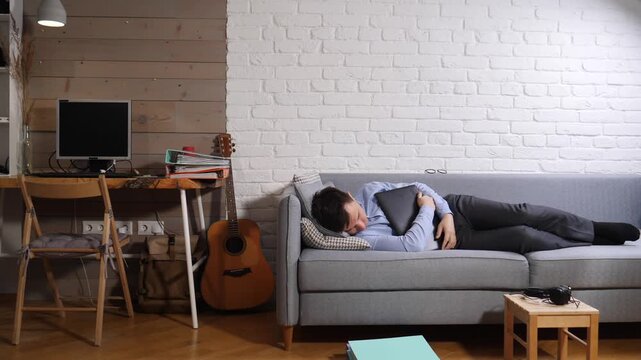 Man yawns on a comfortable sofa with a laptop, showing exhaustion and fatigue from prolonged work, highlighting the challenges of work life balance and remote working