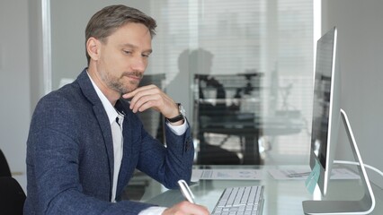 Businessman in a blue jacket thinking and brainstorming ideas while working on computer and taking...